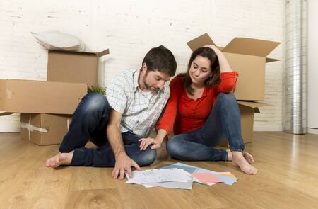 young happy American couple sitting on floor cuddling and celebrating moving in a new house or...