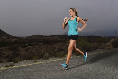 young attractive and fit sport woman running outdoors on asphalt road in mountain landscape on...