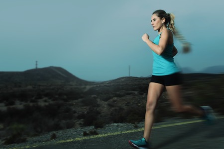 young attractive and fit sport woman running outdoors on asphalt road in mountain landscape on evening with harsh light in fitness workout training shot in motion blurred advertising styleの写真素材