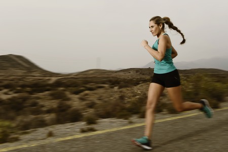 young attractive and fit sport woman running outdoors on asphalt road in mountain landscape on evening with harsh light in fitness workout training shot in motion blurred advertising styleの写真素材