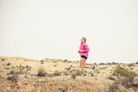 young attractive sport woman running on off road trail dirty road with dry desert landscape...