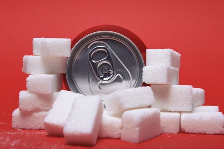 cola refreshing drink can and lot of white sugar cubes representing the big amount of calories content in the soda in unhealthy nutrition concept isolated on red backgroundの写真素材