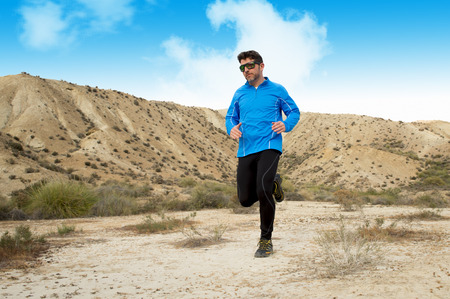 young sport man running on dry desert landscape wearing sunglasses under a blue sky in fitness healthy lifestyle and jogging training workout conceptの写真素材