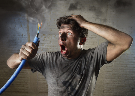 young man holding electrical cable smoking after domestic accident with dirty burnt face in funny sad expression in electricity DIY repairs danger concept  in black smoke backgroundの写真素材