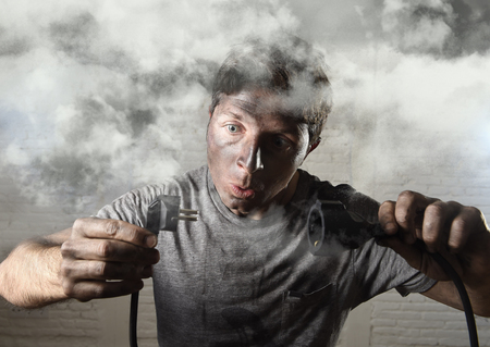 young untrained man joining electrical cable suffering domestic accident with dirty burnt face in funny shock expression screaming crazy in electricity DIY repairs danger conceptの写真素材