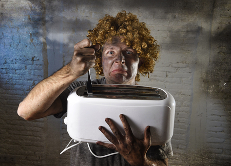 young man electrocuted trying to get toast out of toaster with knife suffering domestic accident with dirty burnt face in funny shock expression screaming crazy in electricity danger conceptの写真素材