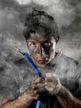 young untrained man joining electrical cable suffering domestic accident with dirty burnt face in funny shock expression screaming crazy in electricity DIY repairs danger conceptの写真素材