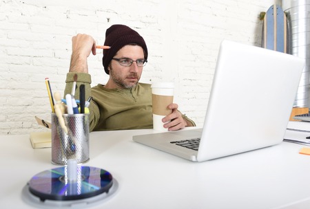 young attractive hipster businessman holding take away coffee working from his home office as freelancer wearing beanie looking busy in self employed business model successの写真素材