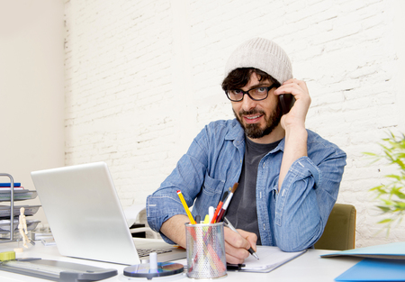 corporate portrait of young hispanic attractive hipster businessman on his 30s working at modern home office with computer laptop talking on mobile phone in freelance business concept corporate portrait of young hispanic attractive hipster businessman on his 30s working at modern home office with computer laptop talking on mobile phone in freelance business concept