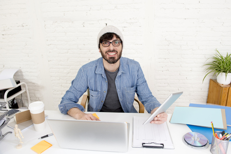 corporate portrait of young hispanic attractive hipster businessman on his 30s working at modern home office with computer laptop using digital tablet pad in creative freelancer conceptの写真素材