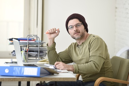 corporate young attractive hipster businessman working with computer laptop at home office as freelancer in casual beanie desk smiling happy and confident  in creative freestyle businessの写真素材