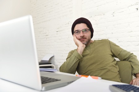 corporate young attractive hipster businessman working with computer laptop at home office as freelancer in casual beanie desk smiling happy and confident  in creative freestyle businessの写真素材