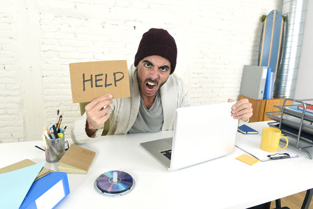 young worried businessman in cool hipster beanie look holding help sign working in stress at home...