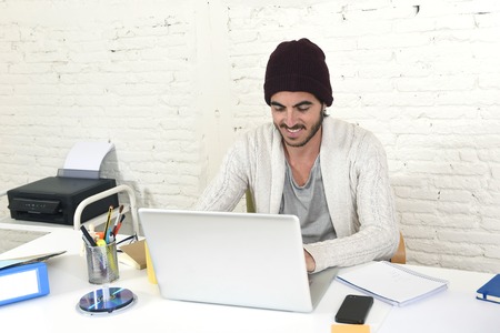young trendy businessman in cool hipster beanie look smiling confident and working happy at modern home office with computer as creative designer in freelance business success conceptの写真素材
