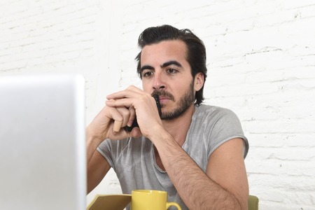 young modern hipster style student and businessman working as freelance creative designer at home office with laptop computer holding mobile phone thinking concentrated analyzing projectの写真素材