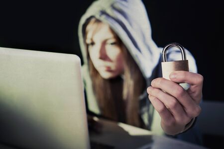 young attractive teen woman wearing hood on looking dark and dangerous hacking laptop computer...