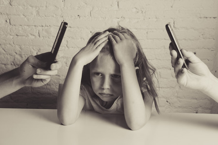 hands of internet and network addict mother and father using mobile phone neglecting little sad ignored daughter bored and lonely feeling abandoned and disappointed in parents bad behaviour conceptの写真素材