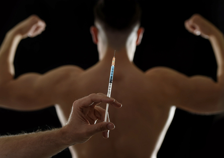 strong back of young body building sportsman using steroids for increasing sport athletic performance and hand holding syringe in sport cheat doping and illegal use of hormones conceptの写真素材