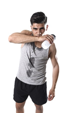 portrait of young athletic sport man thirsty holding bottle of water  with sweaty face and wet singlet after refreshing and recovering after hard training workout in hydration conceptの写真素材