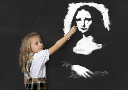 sweet junior schoolgirl with blonde hair drawing and painting with chalk La Gioconda amazing replica in classroom blackboard wearing school uniform in children art education and artistic talentの写真素材