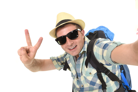 young attractive man or backpacker student taking selfie photo alone with mobile phone or camera wearing sunglasses and summer hat in tourist look smiling happy isolated on white backgroundの写真素材