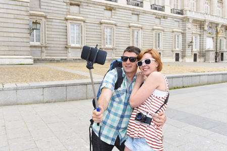 young attractive American couple enjoying holiday trip in Spain taking selfie photo self portrait with mobile phone smiling happy having fun wearing traveler clothes carrying backpackの写真素材