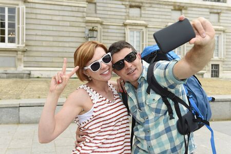young attractive American couple enjoying holiday trip in Spain taking selfie photo self portrait with mobile phone smiling happy having fun wearing traveler clothes carrying backpackの写真素材