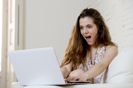 young beautiful woman using laptop computer laughing happy watching something funny or doing online internet shopping at home modern living room in cheerful and satisfied face expressionの写真素材