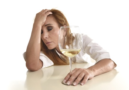 caucasian blond wasted and depressed alcoholic woman drinking white wine glass looking desperate and sad isolated on white in alcohol abuse and addiction and drunk housewife alcoholism problemの写真素材