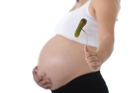 young pregnant woman holding her big belly in one hand and fork with pickle isolated on white background in pregnancy whim food concept isolated on white backgroundの写真素材