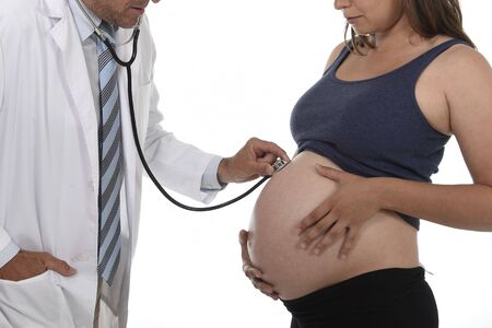 man in medicine doctor coat using stethoscope listening to fetus heartbeat in  pregnant woman big belly in health care and motherhood concept isolated on white backgroundの写真素材