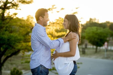 young happy beautiful couple in love walking together on grass and trees park landscape on sunset in summer with pregnant cheerful wife and husband looking at each other in family conceptの写真素材