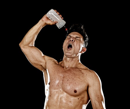 attractive strong sport man pouring water on his face sweating tired after training hard on gym bodybuilding workout isolated on black background in health care hydration and fitness conceptの写真素材