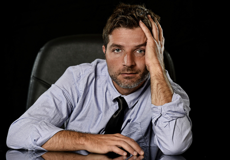 young attractive businessman in worried tired and stressed face expression sitting depressed isolated on office chair with black background in overwork overtime and stress at work conceptの写真素材