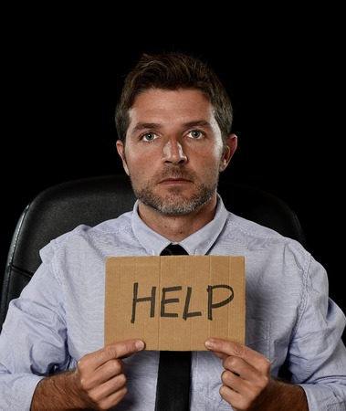 young attractive businessman in worried tired and stressed face expression sitting depressed isolated on office chair with black background in overwork overtime asking for help in stress conceptの写真素材