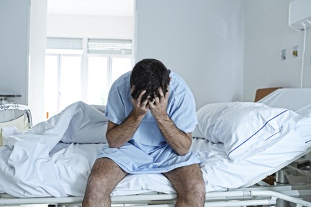 young desperate man sitting at hospital bed alone sad and devastated suffering depression crying at clinic for serious disease diagnose feeling worried and in fear about healthの写真素材