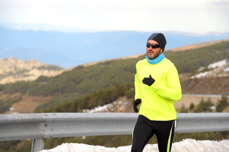 young healthy sport man running on asphalt road at snow mountains in trail runner hard workout in...