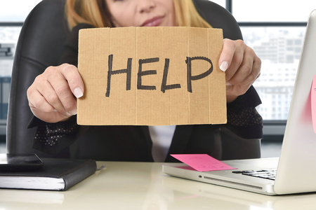 frustrated attractive businesswoman in her 40s holding help sign desparate suffering stress overworked and overwhelmed working at office laptop computer in sad and worried face expressionの写真素材
