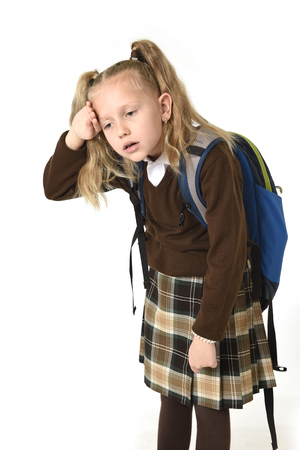 sweet beautiful little schoolgirl tired and exhausted carrying on her back heavy school backpack looking sad and depressed in weight of school books concept isolated on whiteの写真素材