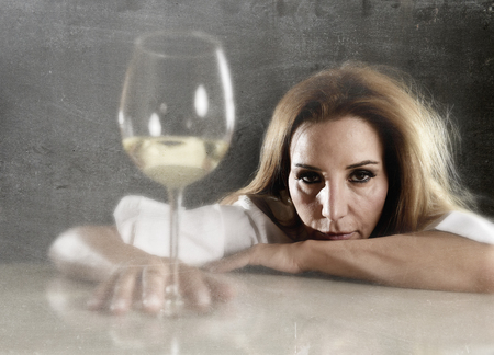drunk blond woman alone in wasted depressed expression looking thoughtful with white wine glass on grunge dirty background in alcohol abuse and alcoholic housewife conceptの写真素材