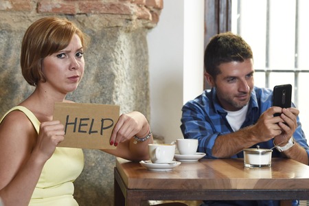 young American couple at coffee shop with internet and mobile phone addict man ignoring bored sad and frustrated woman girlfriend or wife in relationship problem and addiction conceptの写真素材
