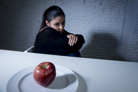 young woman or teen looking apple fruit on dish as symbol of crazy diet in nutrition disorder concept anorexia and bulimia and refusing to eat food in diet calories obsessionの写真素材