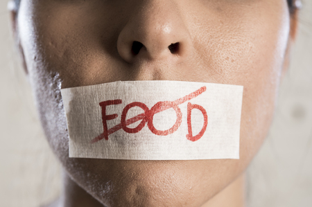 close up face of young beautiful sad latin woman with mouth sealed on stick tape with the text no food and concept of refusing eating and overweight in anorexia bulimia and nutrition disorder conceptの写真素材