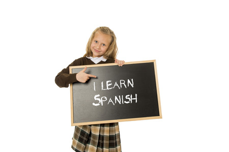7  8 years old little beautiful blond schoolgirl smiling happy and cheerful holding and showing small blackboard with text I learn Spanish in language education concept isolated whiteの写真素材