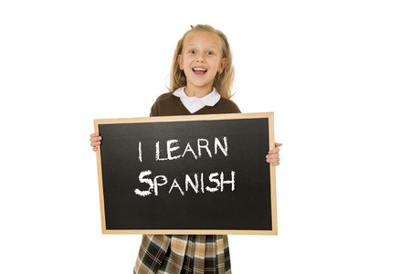 7  8 years old little beautiful blond schoolgirl smiling happy and cheerful holding and showing small blackboard with text I learn Spanish in language education concept isolated whiteの写真素材