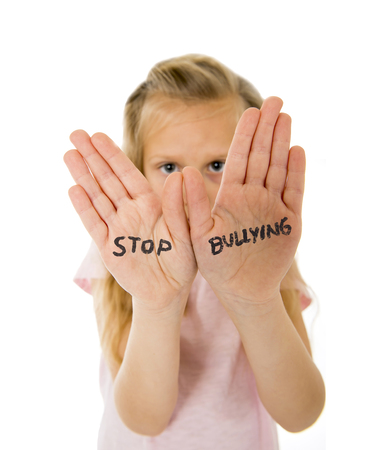 sweet and scared little schoolgirl showing the text stop bullying written in her hands in the concept children bullied and abused in school isolated on white backgroundの写真素材