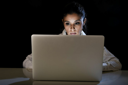 young business woman or student girl working in darkness on laptop computer late at night looking concentrated and tired in long hour of work concept isolated on black backgroundの写真素材
