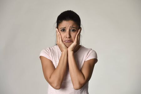 young beautiful hispanic sad woman serious and concerned looking worried and thoughtful facial expression feeling depressed isolated grey background in sadness and sorrow emotionの写真素材
