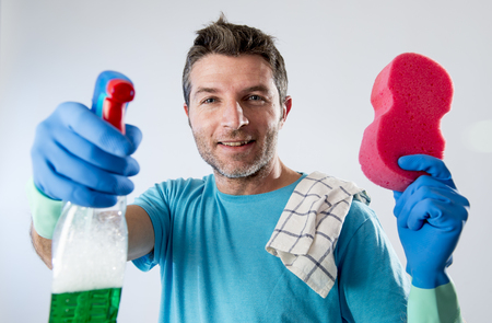 portrait of domestic service man or busy husband smiling happy doing house cleaning with spray bottle and sponge washing glass pointing the camera  isolated even backgroundの写真素材