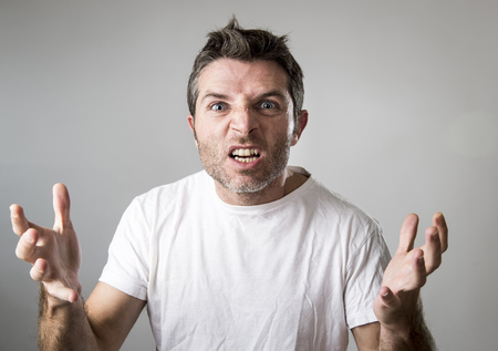 close up portrait of young attractive man with blue eyes looking angry and mad in rage emotion and upset facial expression isolated on grey backgroundの写真素材